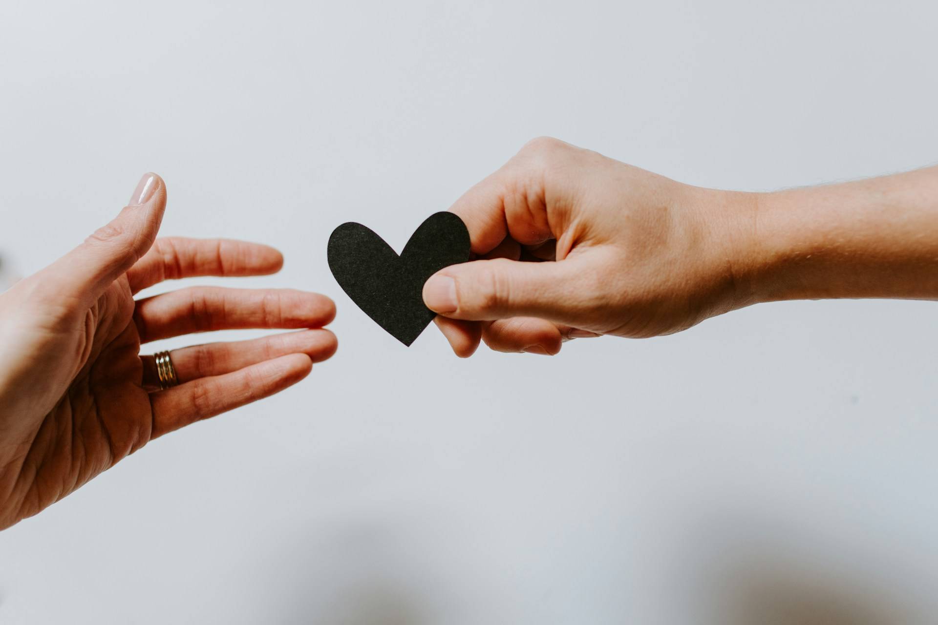 Quelle: unsplash.com / Kelly Sikkema, https://unsplash.com/de/fotos/person-die-schwarzes-herz-ausschnittpapier-erreicht-XX2WTbLr3r8 jemand reicht ein Herz an anderen